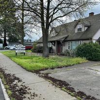 A house is sitting on the corner of a street next to a sidewalk.