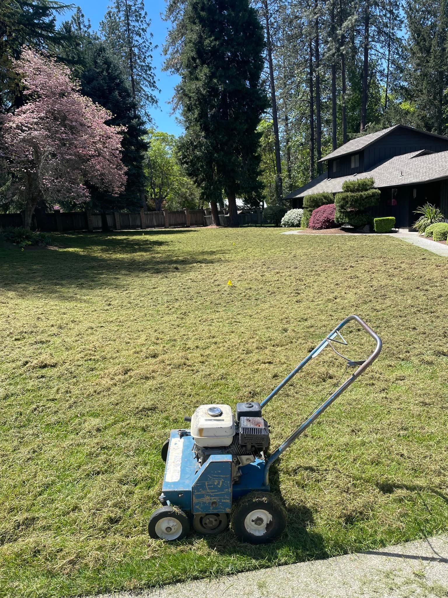 A lawn mower is sitting on the side of a lush green lawn in front of a house.