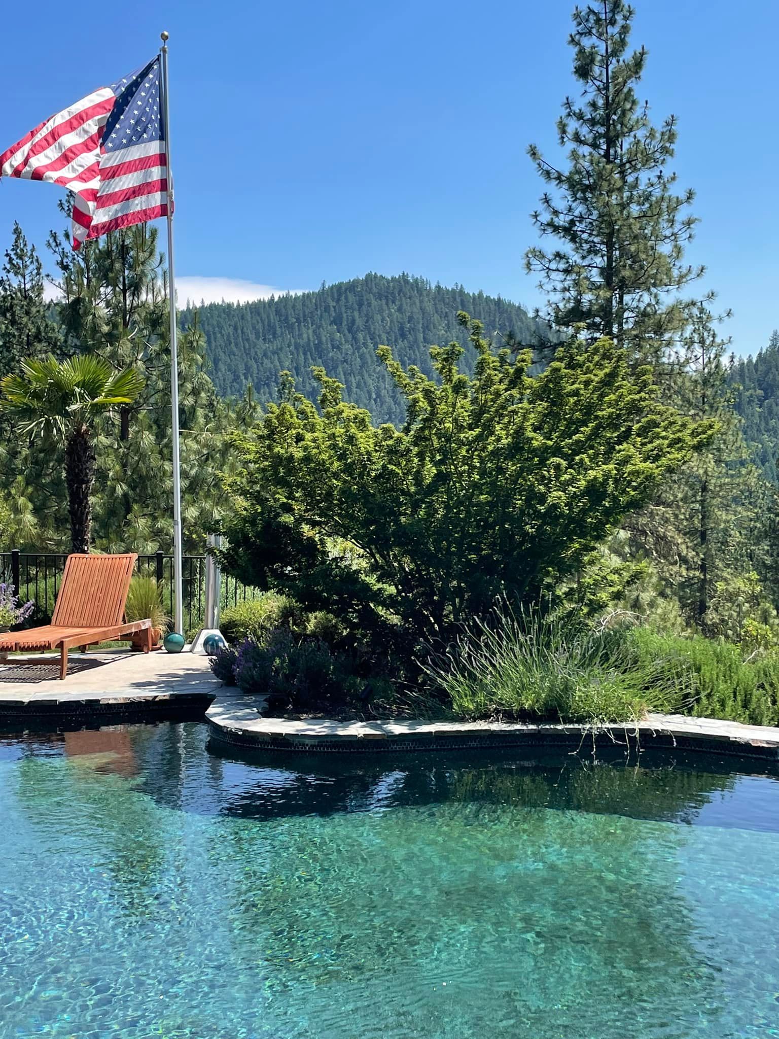 An american flag is flying over a swimming pool with mountains in the background.