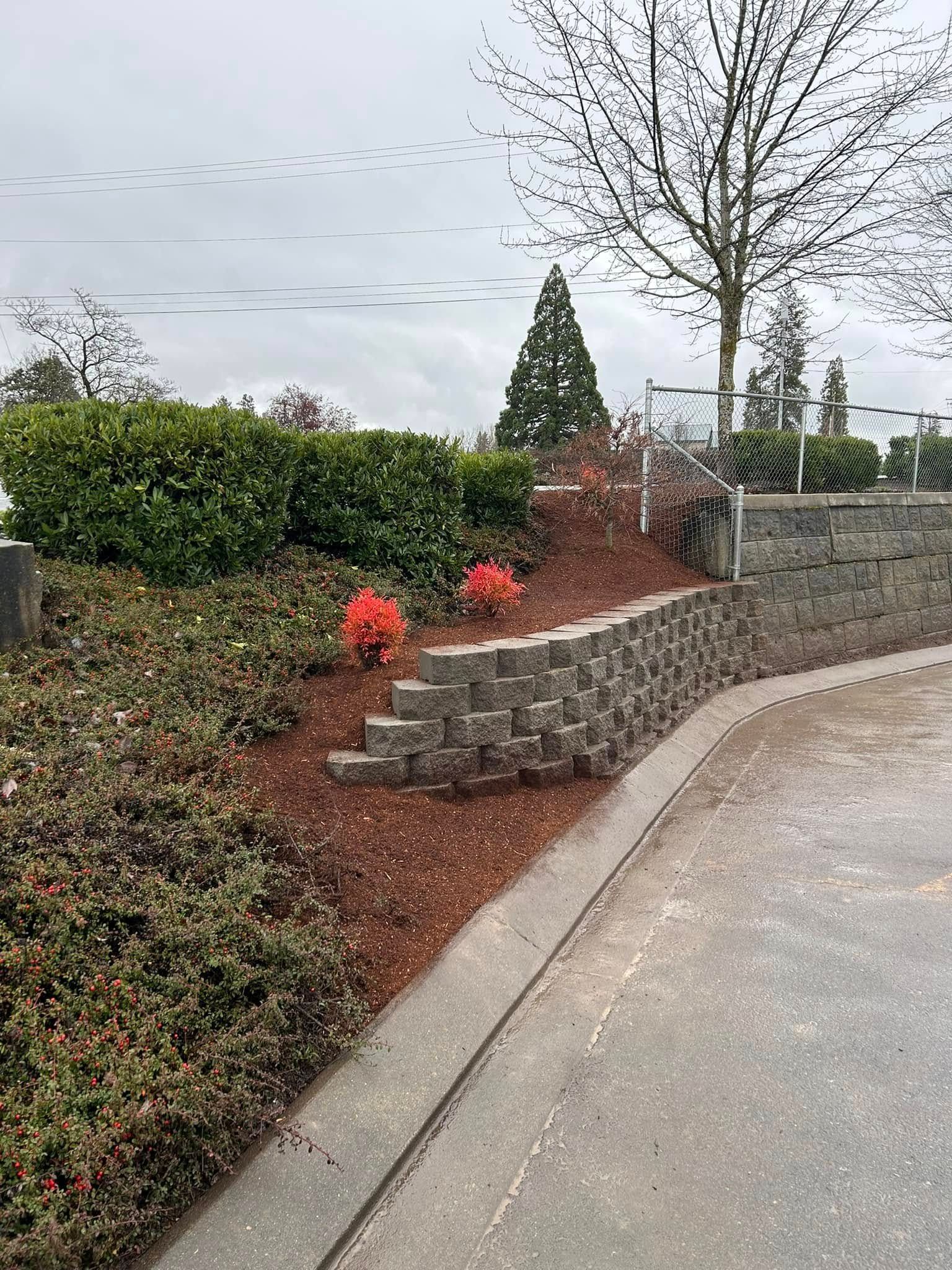A stone wall surrounded by bushes and trees next to a road.