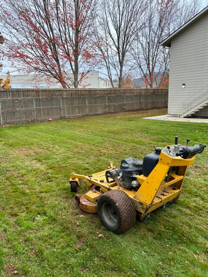 A yellow lawn mower is parked in the grass in front of a house.