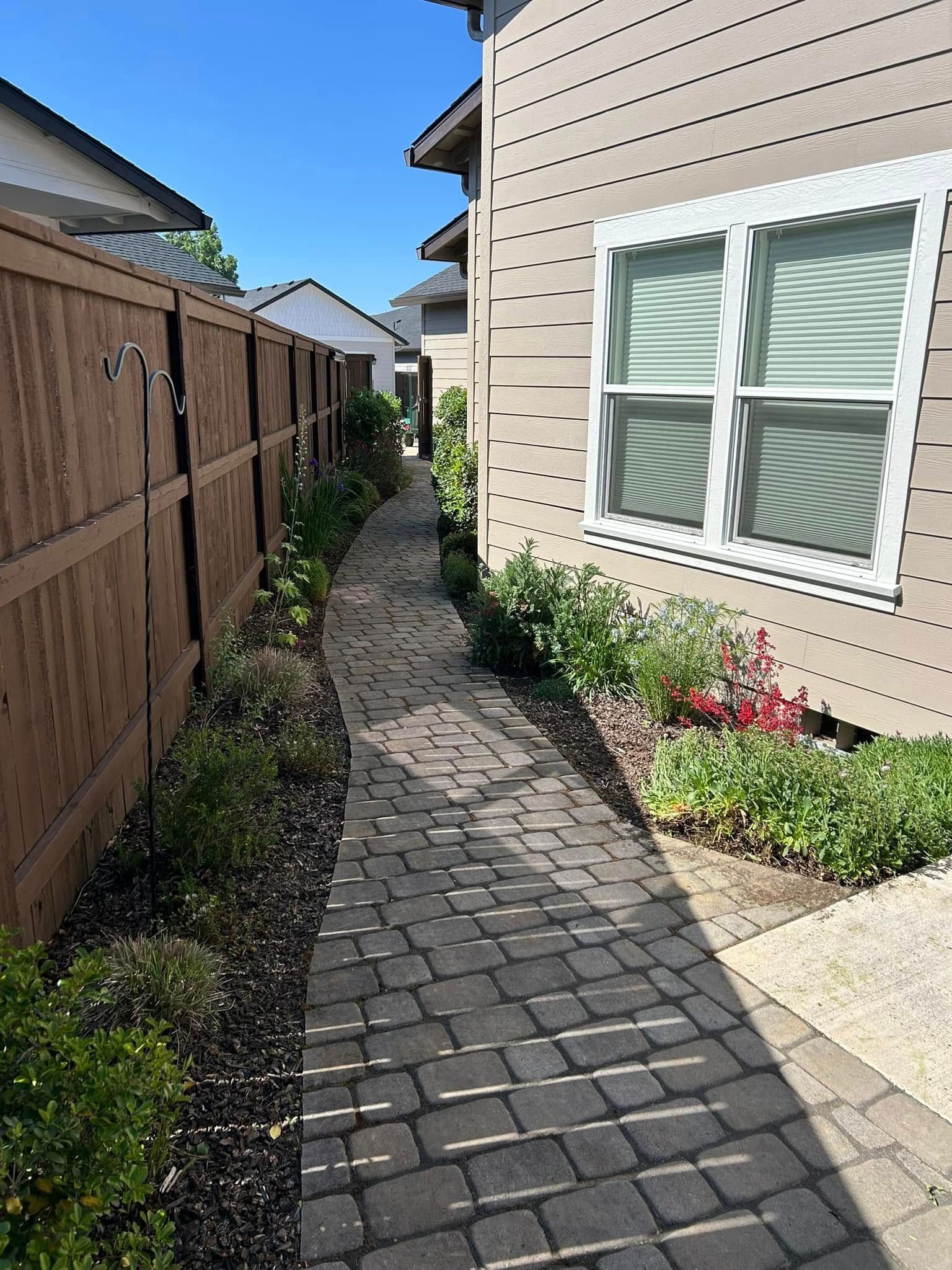 A brick walkway leading to a house with a wooden fence and a window.