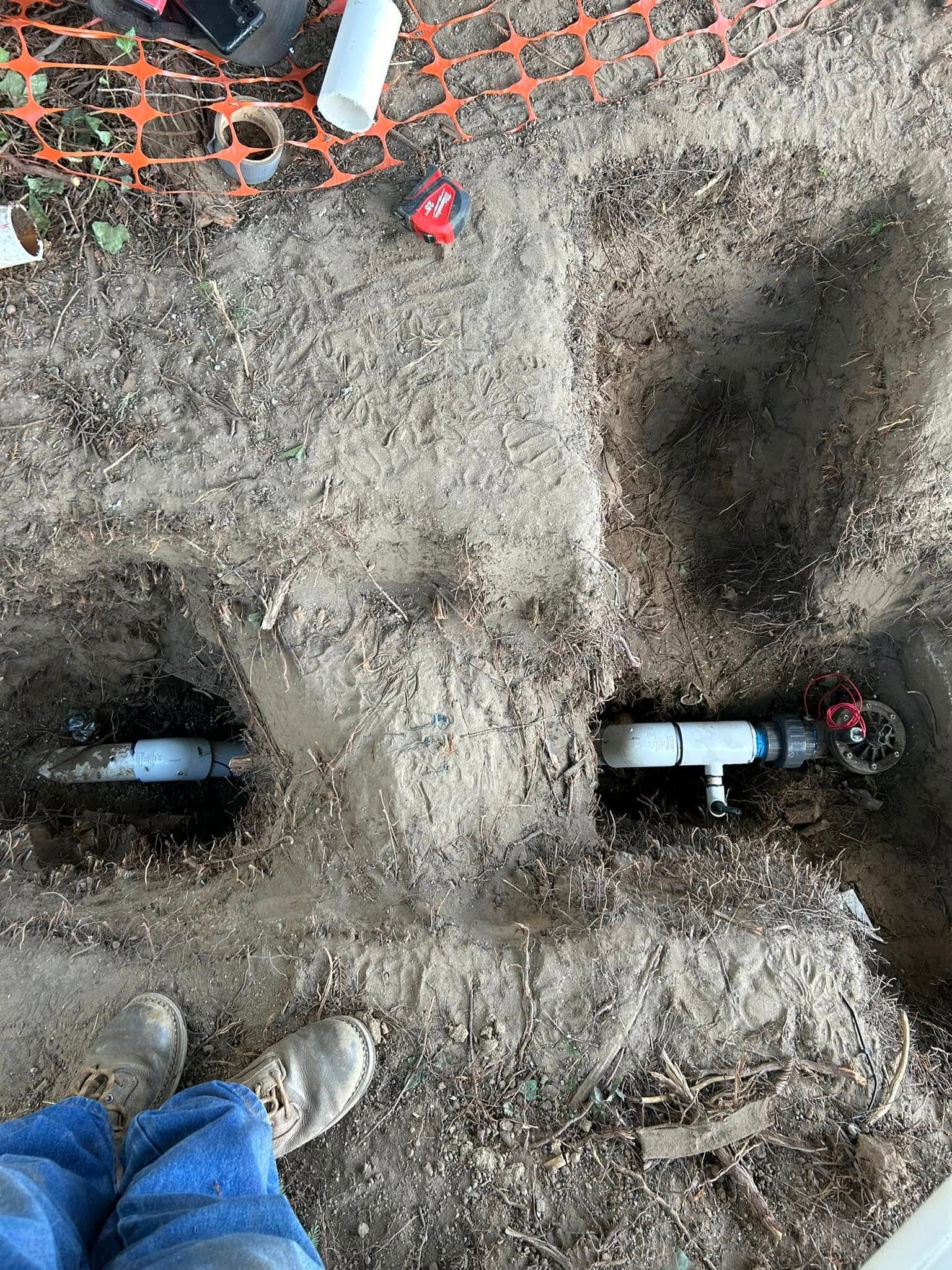 A person is standing in the dirt next to a pipe in the ground.