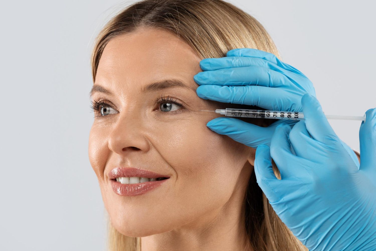 Woman receiving an injection near her eye, blue gloved hands, neutral background.