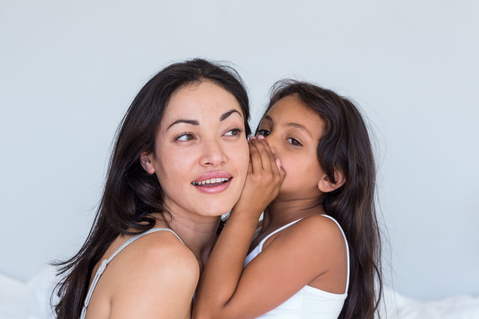 A little girl is whispering a secret into a woman 's ear.