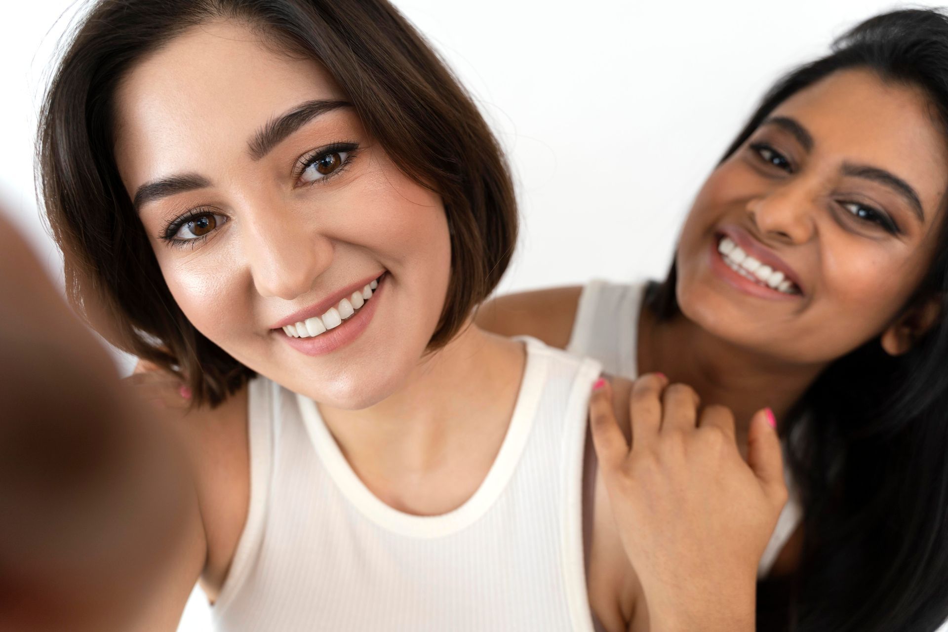 Two women are taking a selfie together and smiling, flaunting their white teeth.