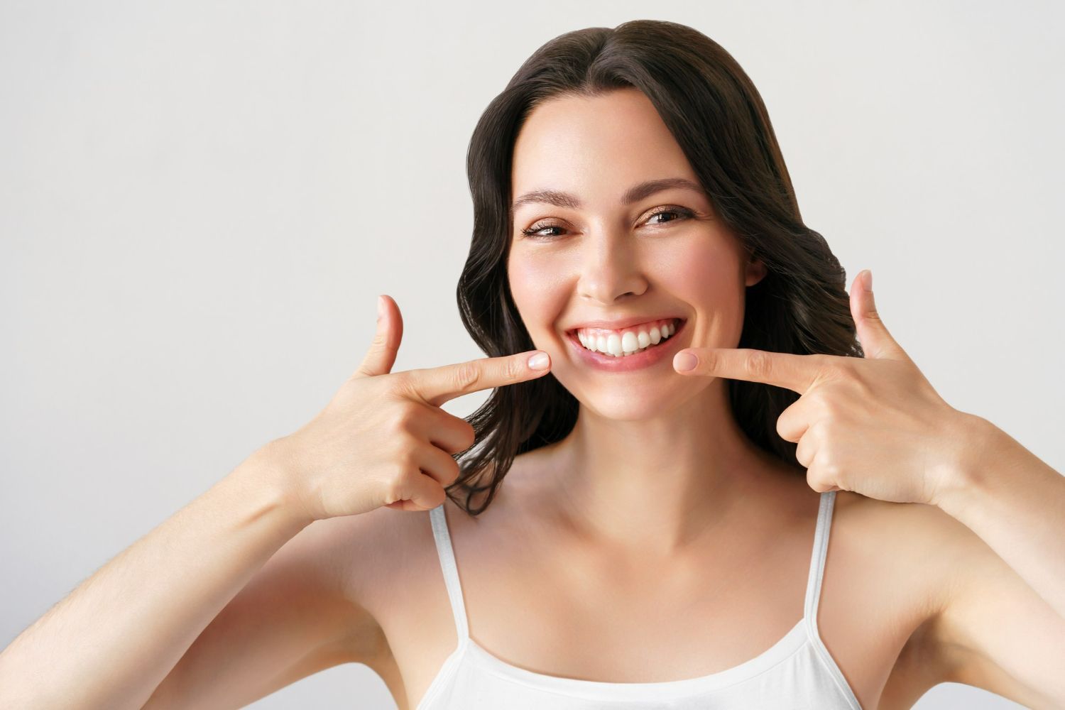 Woman smiling widely, pointing to her teeth. White background.