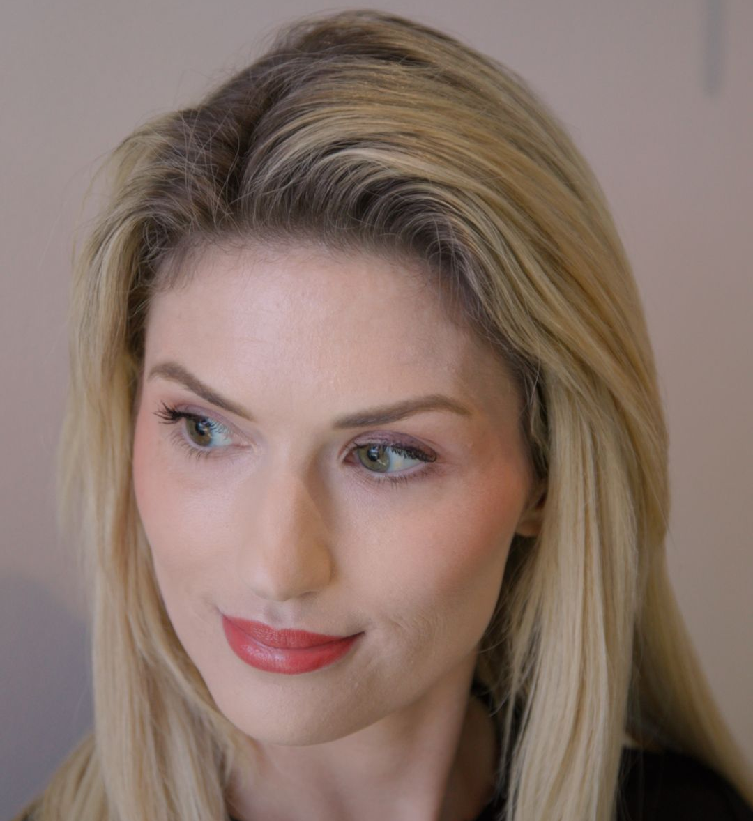 Blonde woman with subtle makeup and coral lipstick looks to the side.