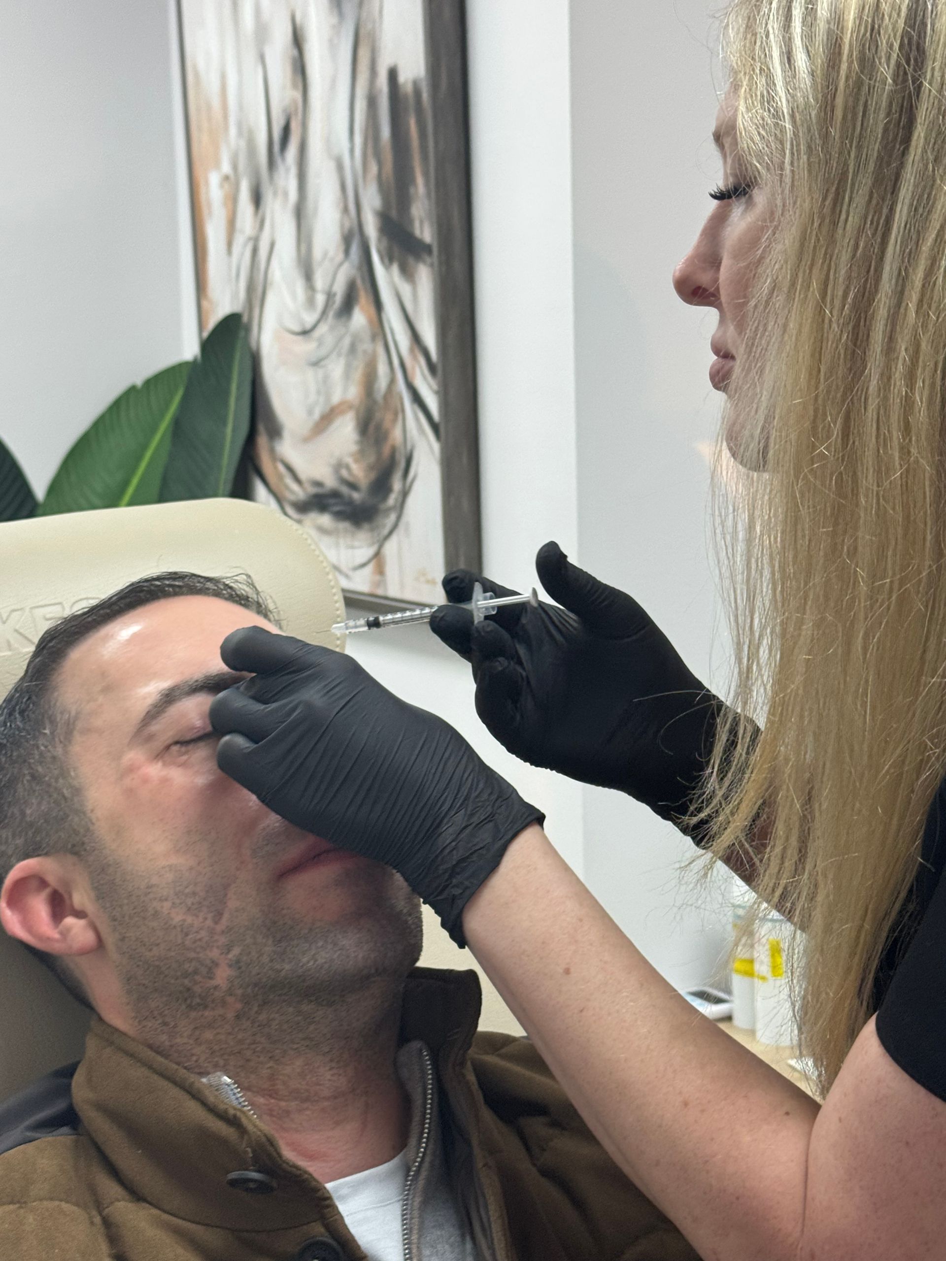 Person receiving an injection in their face from a person wearing black gloves in a medical setting.