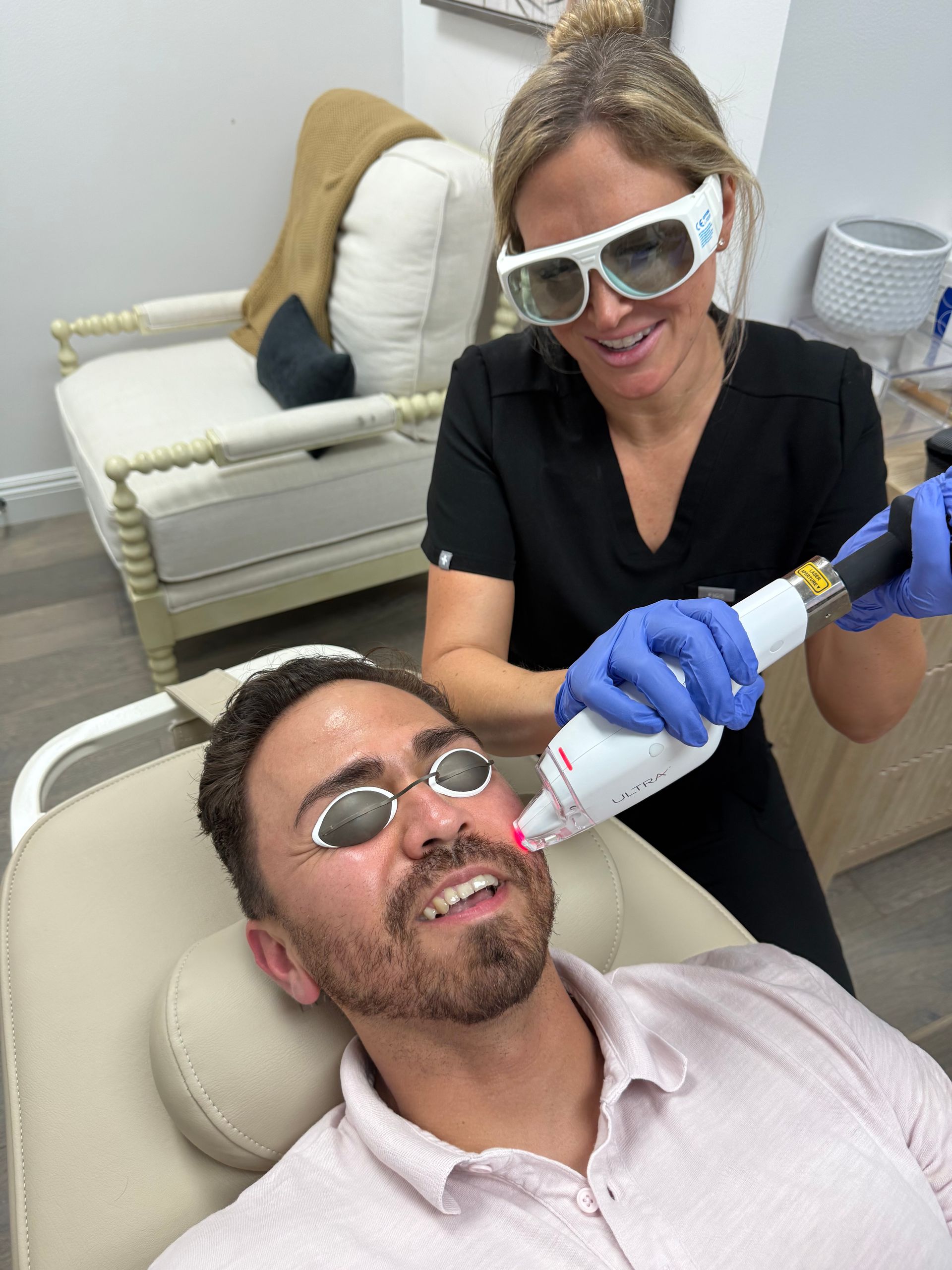 A person receiving laser treatment on their face in a medical setting. A clinician holds a device near the person's face.