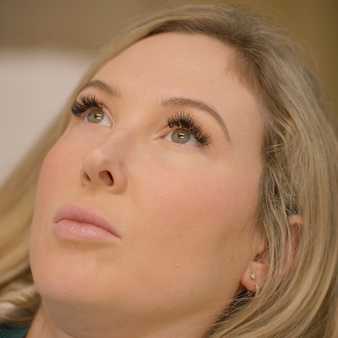 A close up of a woman 's face with long eyelashes looking up.