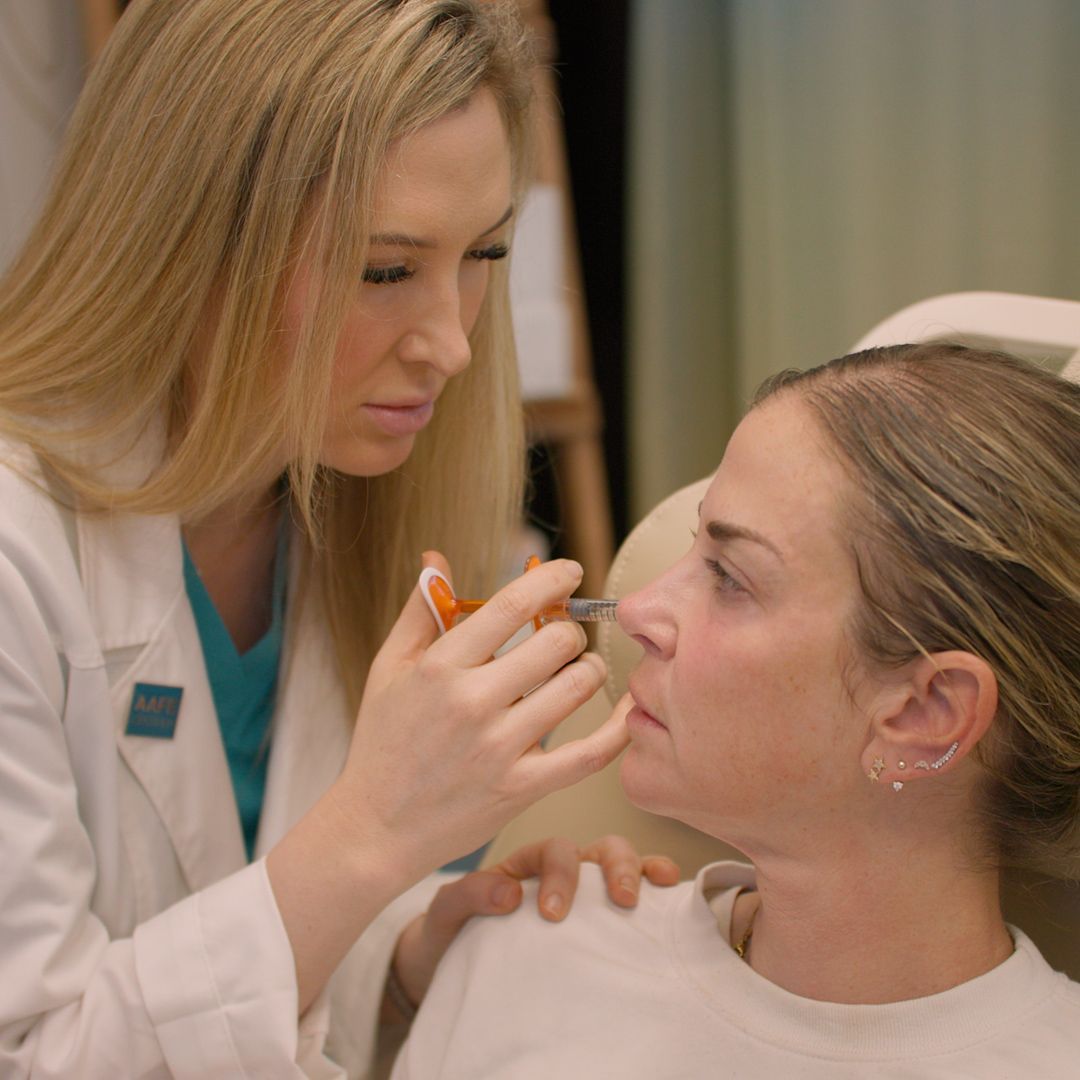 A woman in a white coat is applying makeup to another woman 's face.