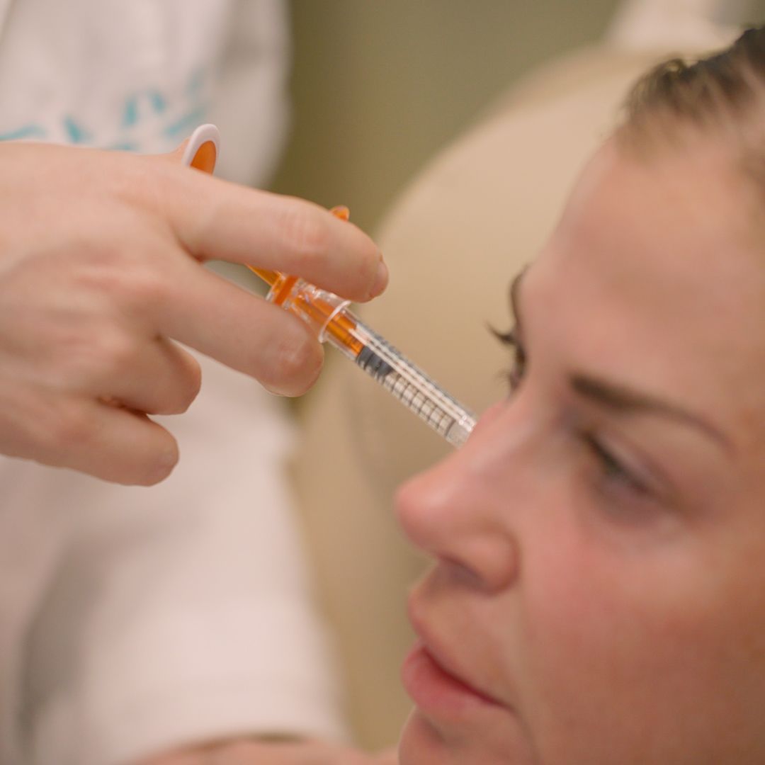 A woman is getting a botox injection in her forehead