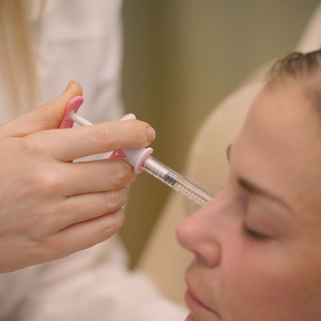 A woman is getting a botox injection in her forehead.