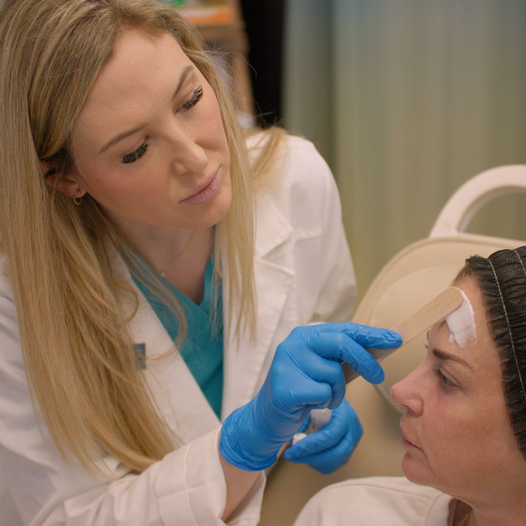 A woman in a white coat and blue gloves is examining a woman 's face.