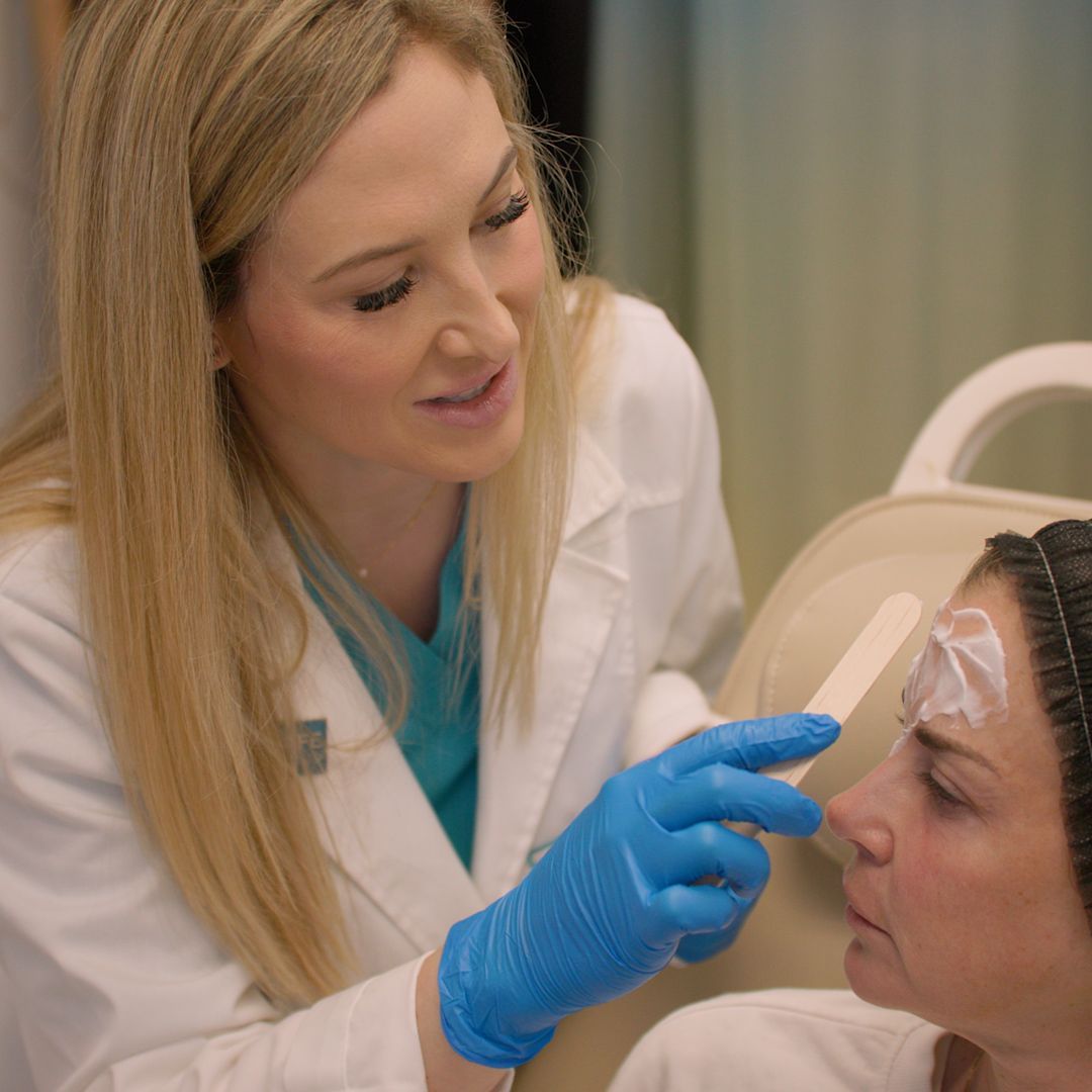 A woman in a white coat and blue gloves is examining a woman 's face.