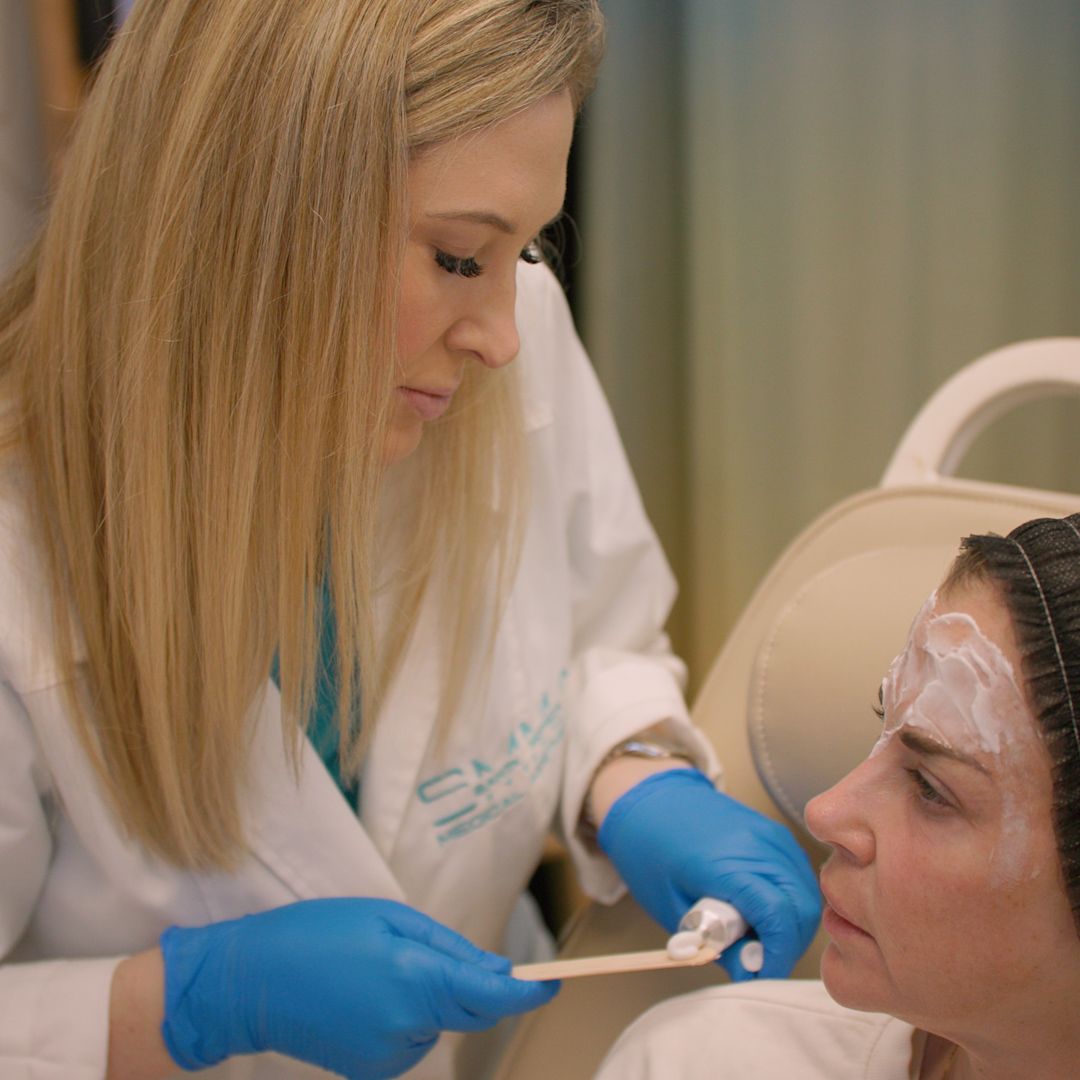 A woman in a white coat and blue gloves is examining a woman 's face