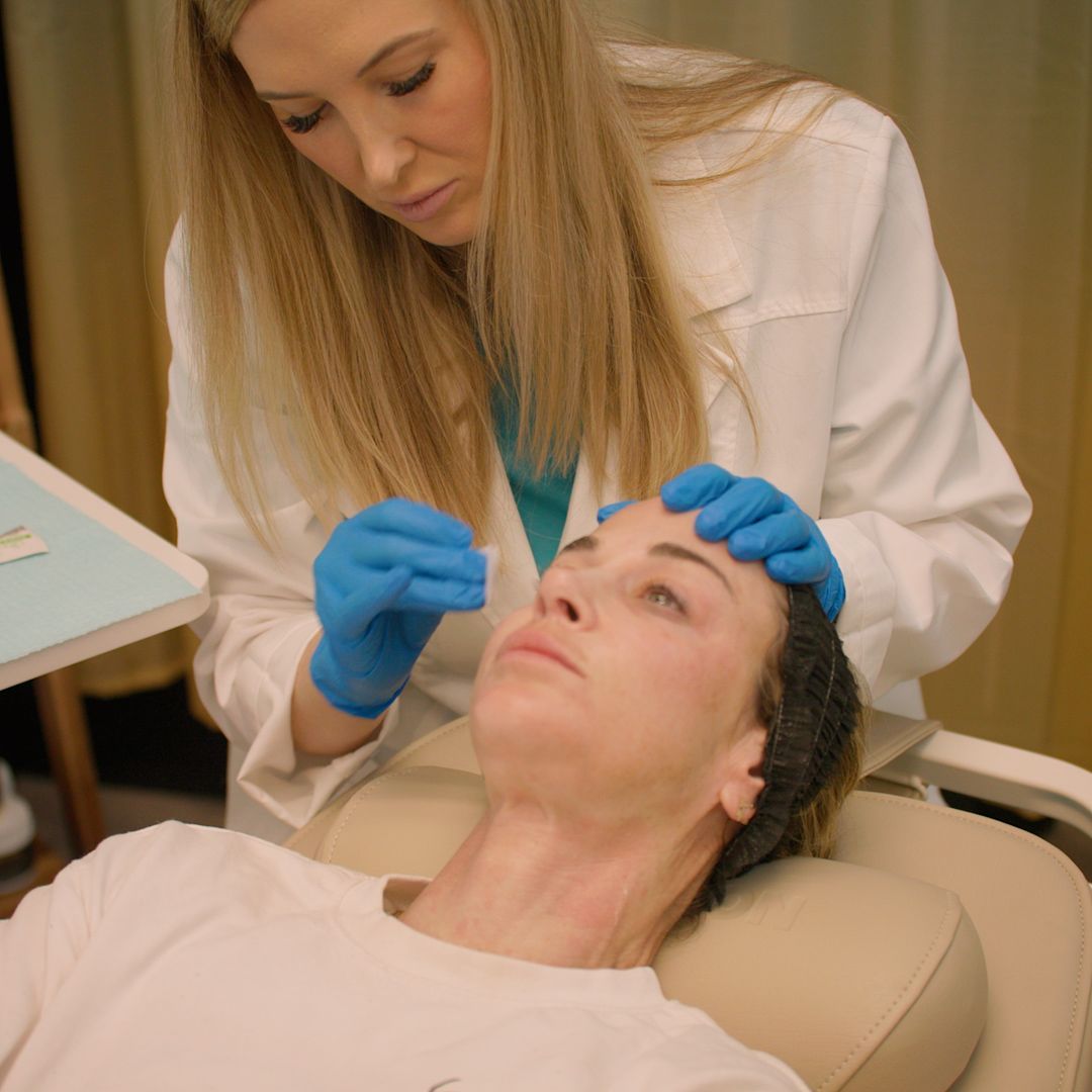 A woman is laying in a chair while a doctor examines her face