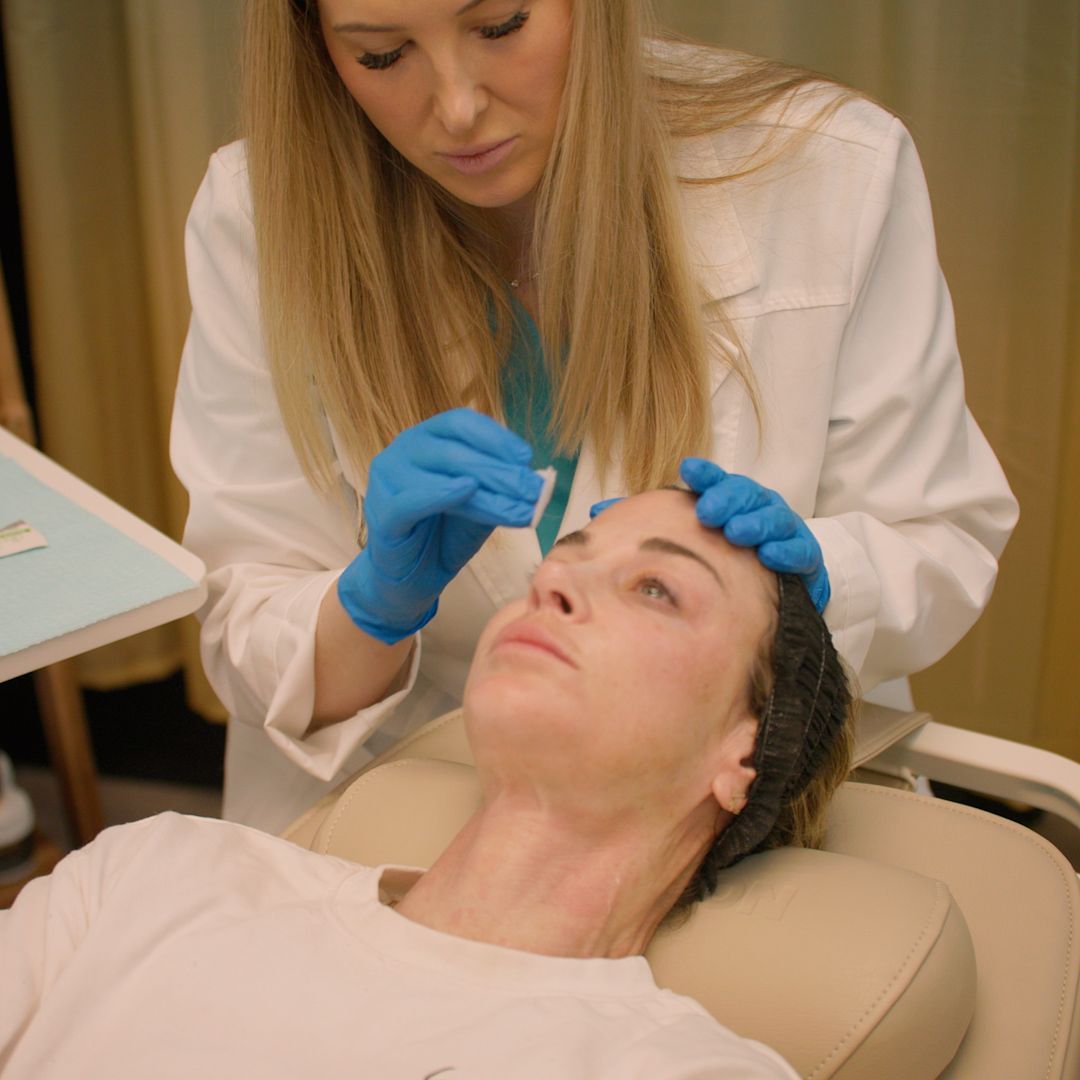 A woman in a white coat and blue gloves is measuring a woman 's nose