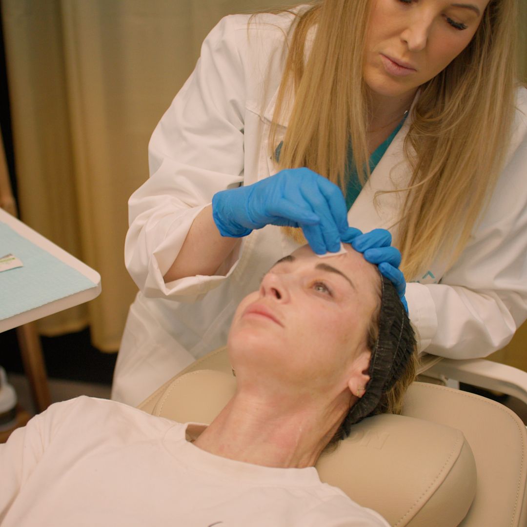 A woman is laying in a chair while a doctor examines her face