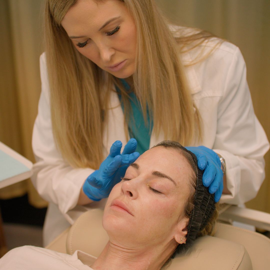 A woman is laying in a chair while a doctor examines her face.