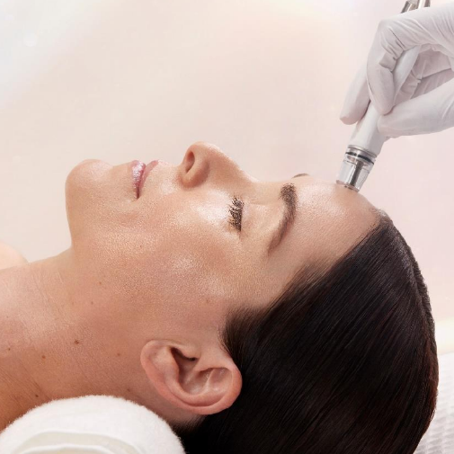 A woman is getting a diamond glow treatment on her forehead.