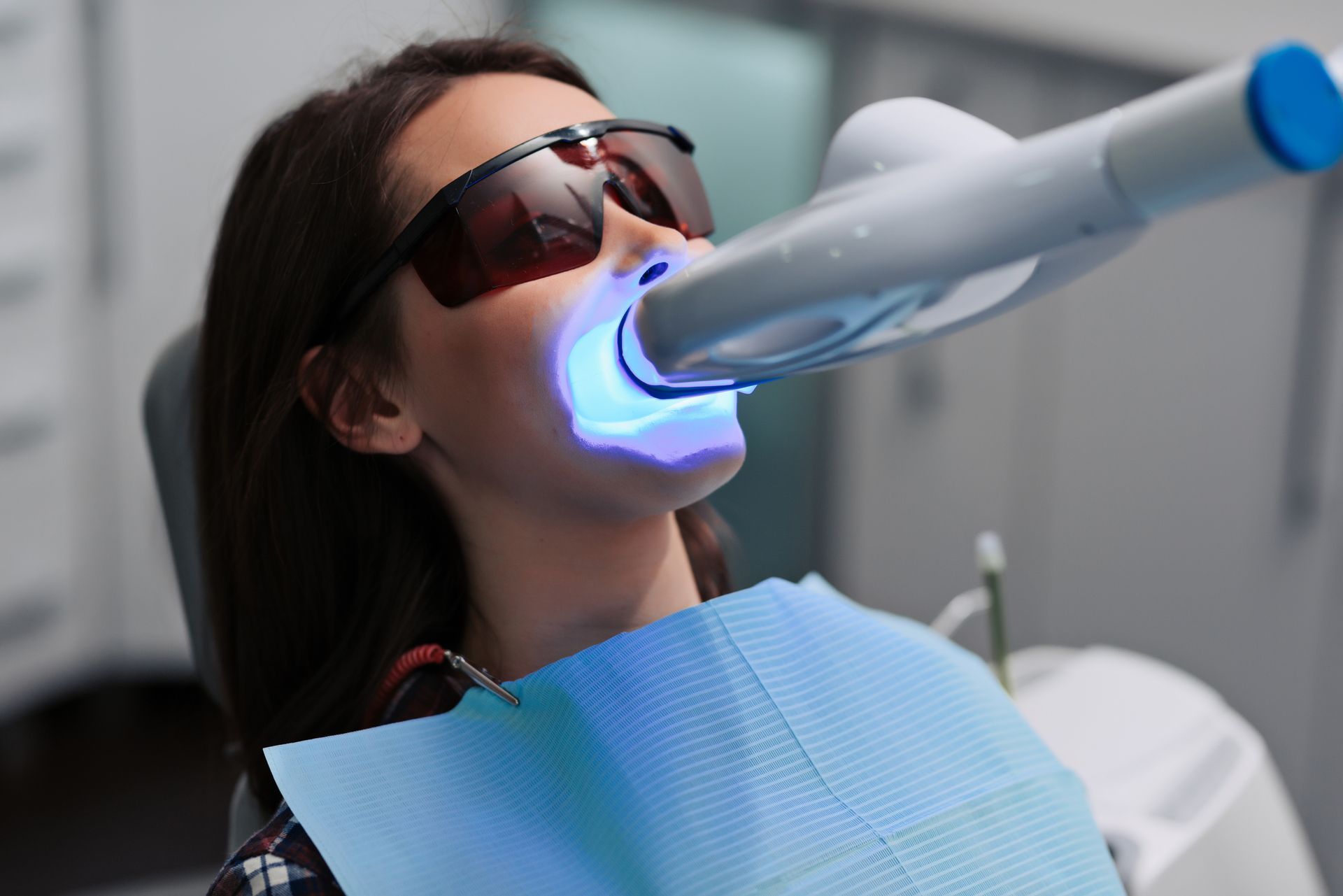 A woman is getting her teeth whitened in a dental office.