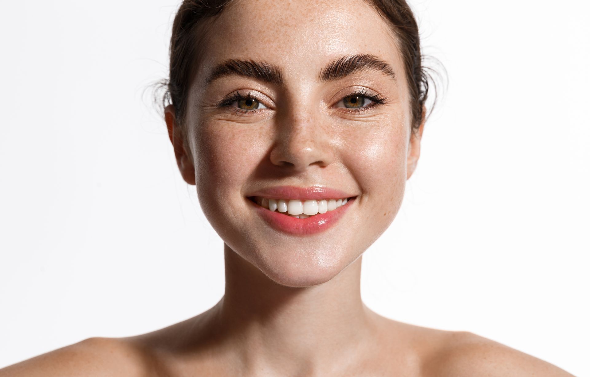 Woman with freckles smiles broadly, highlighting her bright eyes and glossy lips.