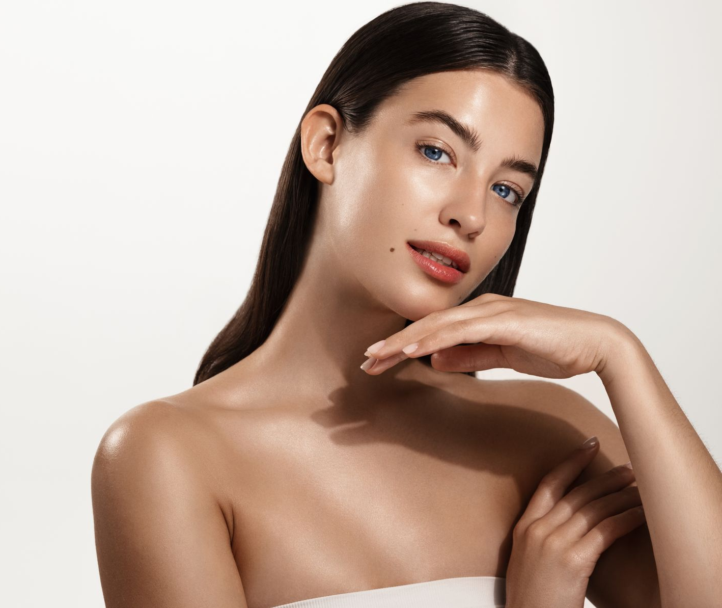 Woman with shiny skin, long dark hair, and hand near face, glowing.