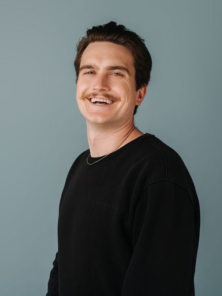 A man with a mustache is wearing a black sweater and smiling.