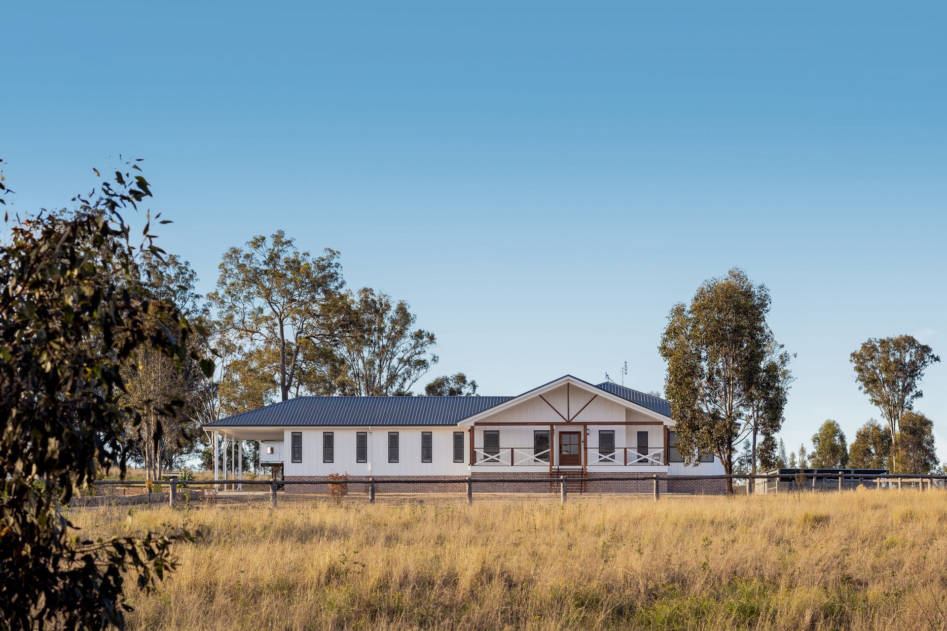 a large white house is sitting in the middle of a field surrounded by trees .