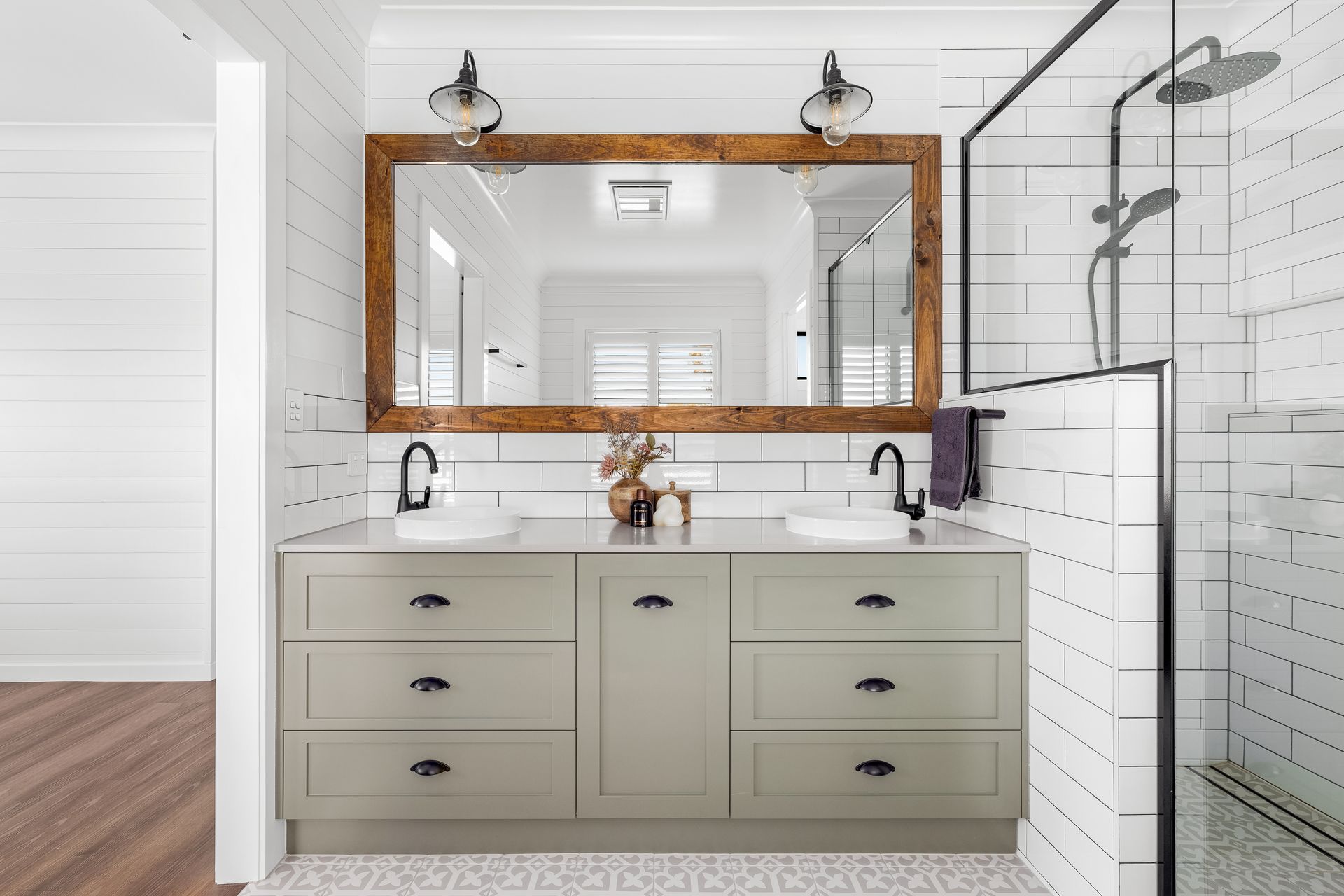 a bathroom with two sinks , a large mirror and a walk in shower .