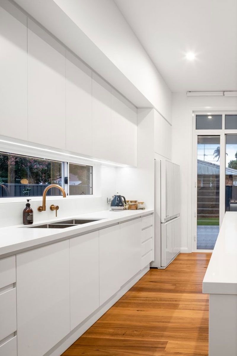 a kitchen with white cabinets , wooden floors , a sink and a refrigerator .