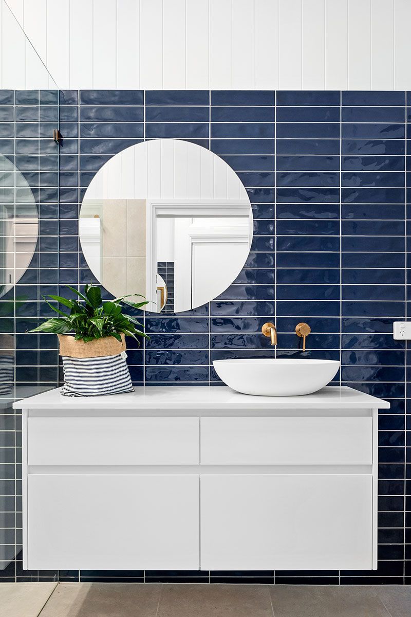 a bathroom with blue tiles , a sink , a mirror and a plant .