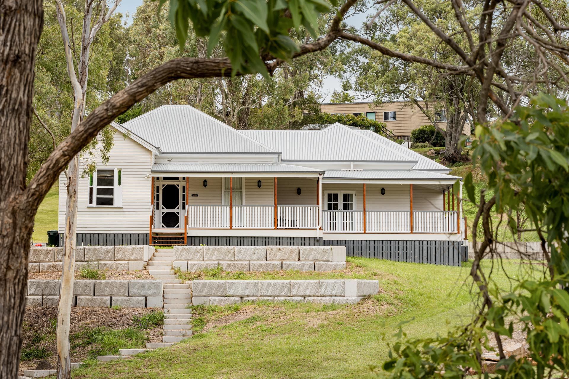A white house with a porch is sitting on top of a grassy hill.