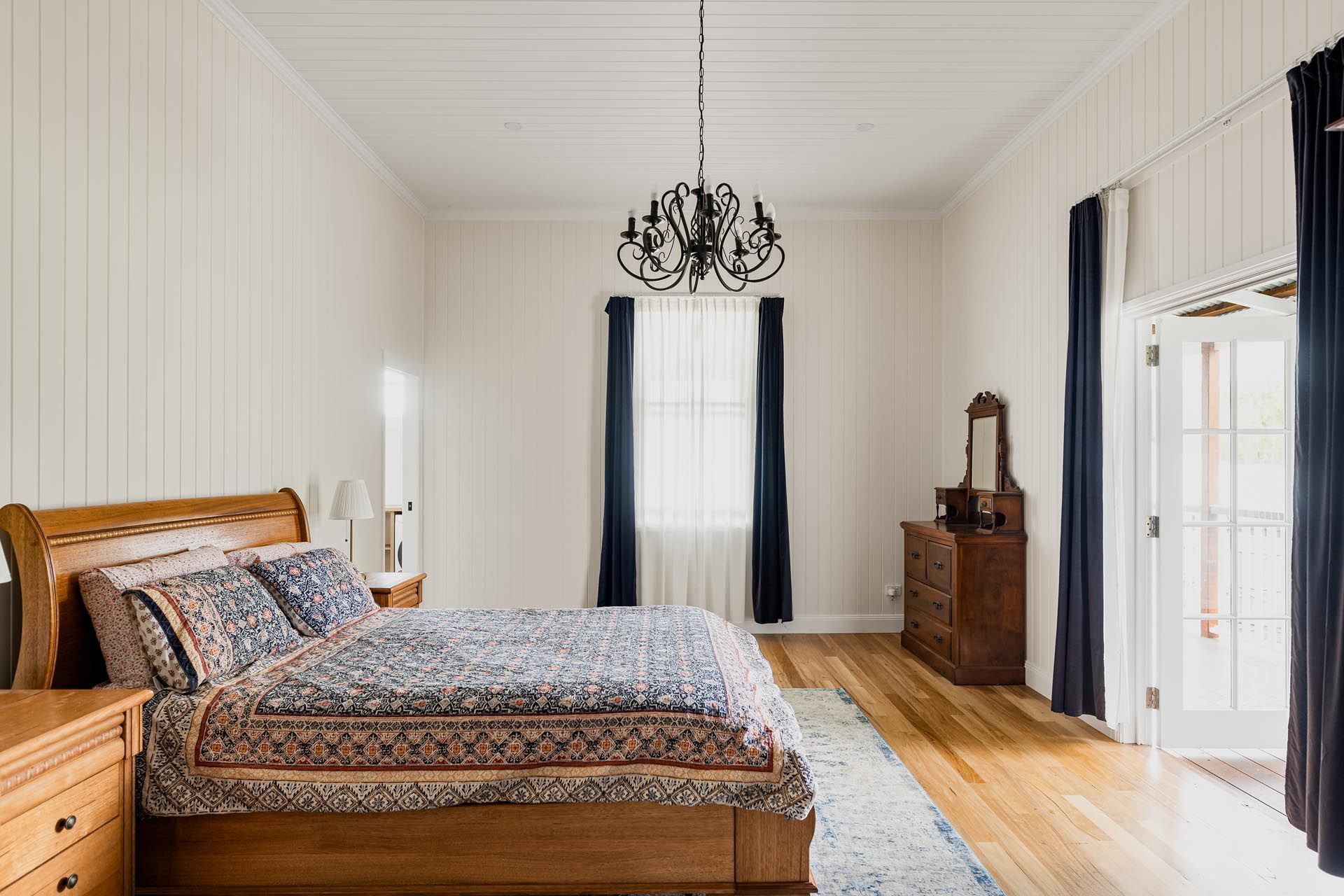 A bedroom with a bed , dresser , mirror and chandelier.