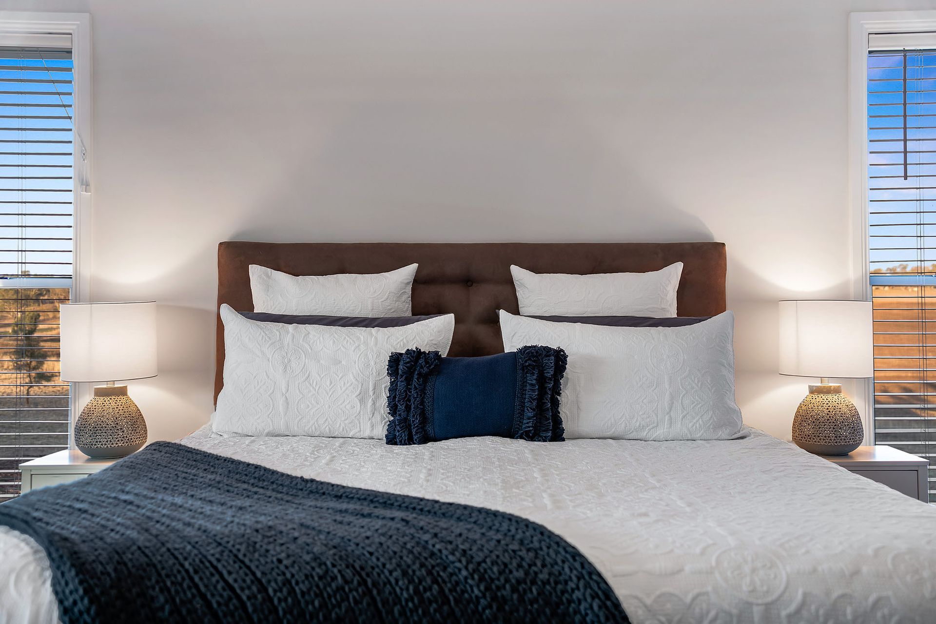 a bedroom with a large bed , two lamps , and two windows .