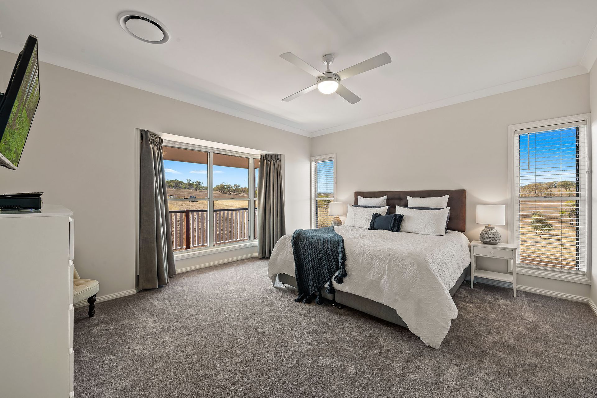 a bedroom with a large bed , a ceiling fan , a television and a balcony .