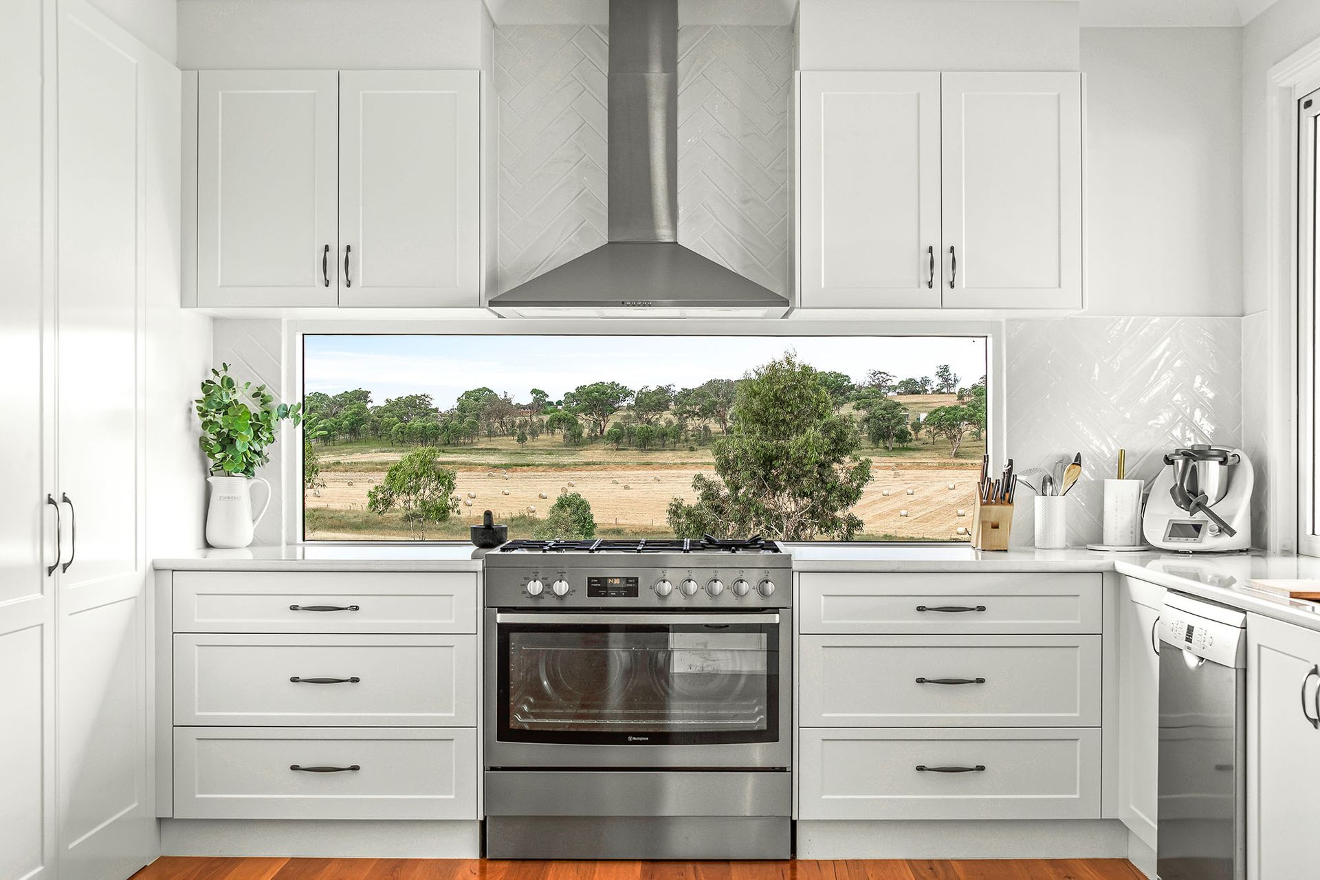 a kitchen with white cabinets , stainless steel appliances and a large window .