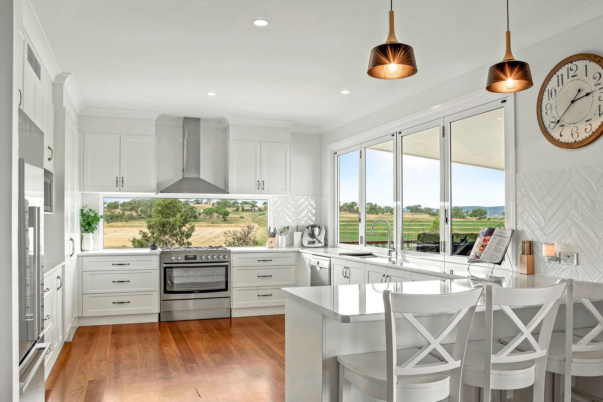a kitchen with white cabinets , stainless steel appliances , hardwood floors and a clock on the wall .