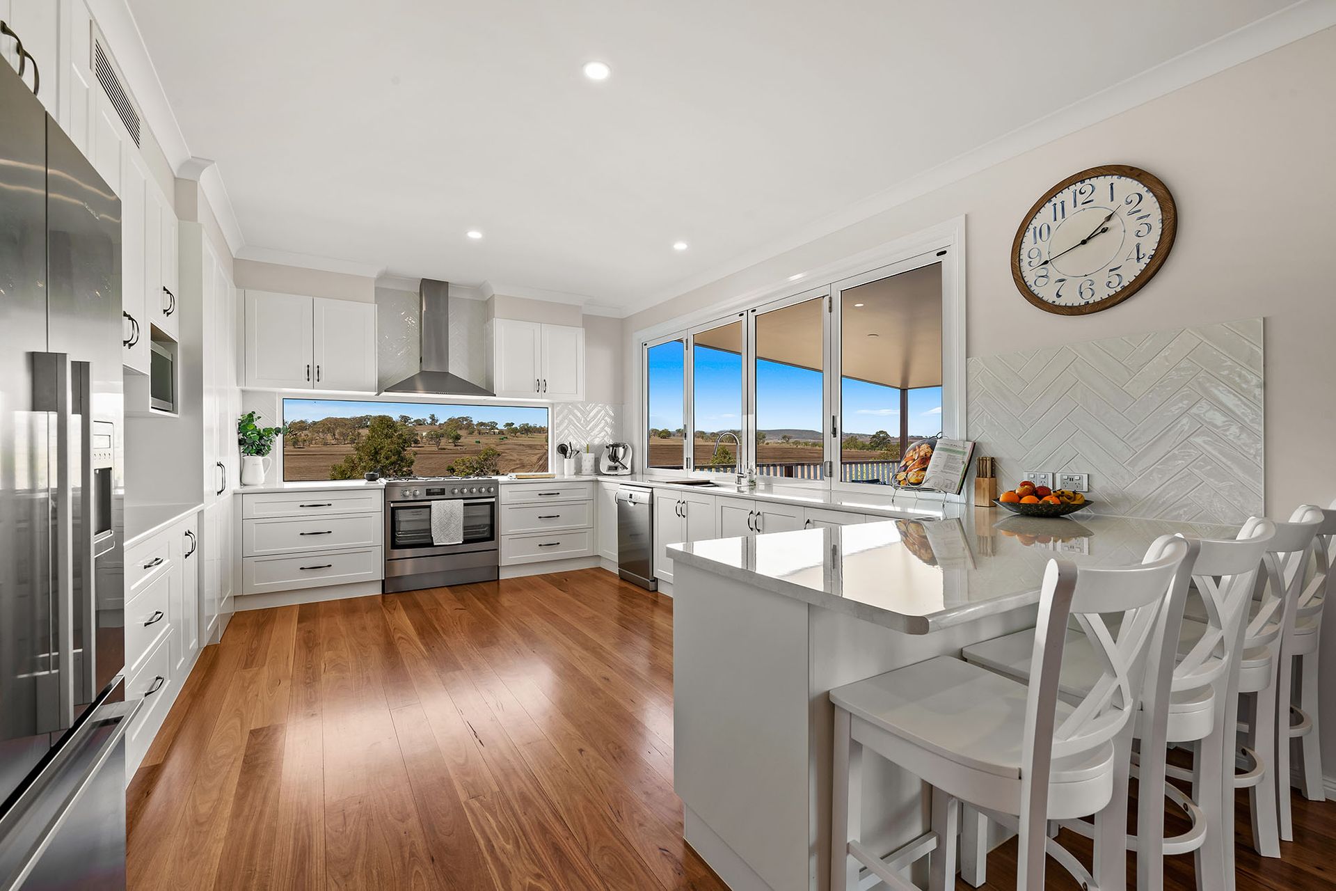 a kitchen with white cabinets , stainless steel appliances , hardwood floors and a clock on the wall .