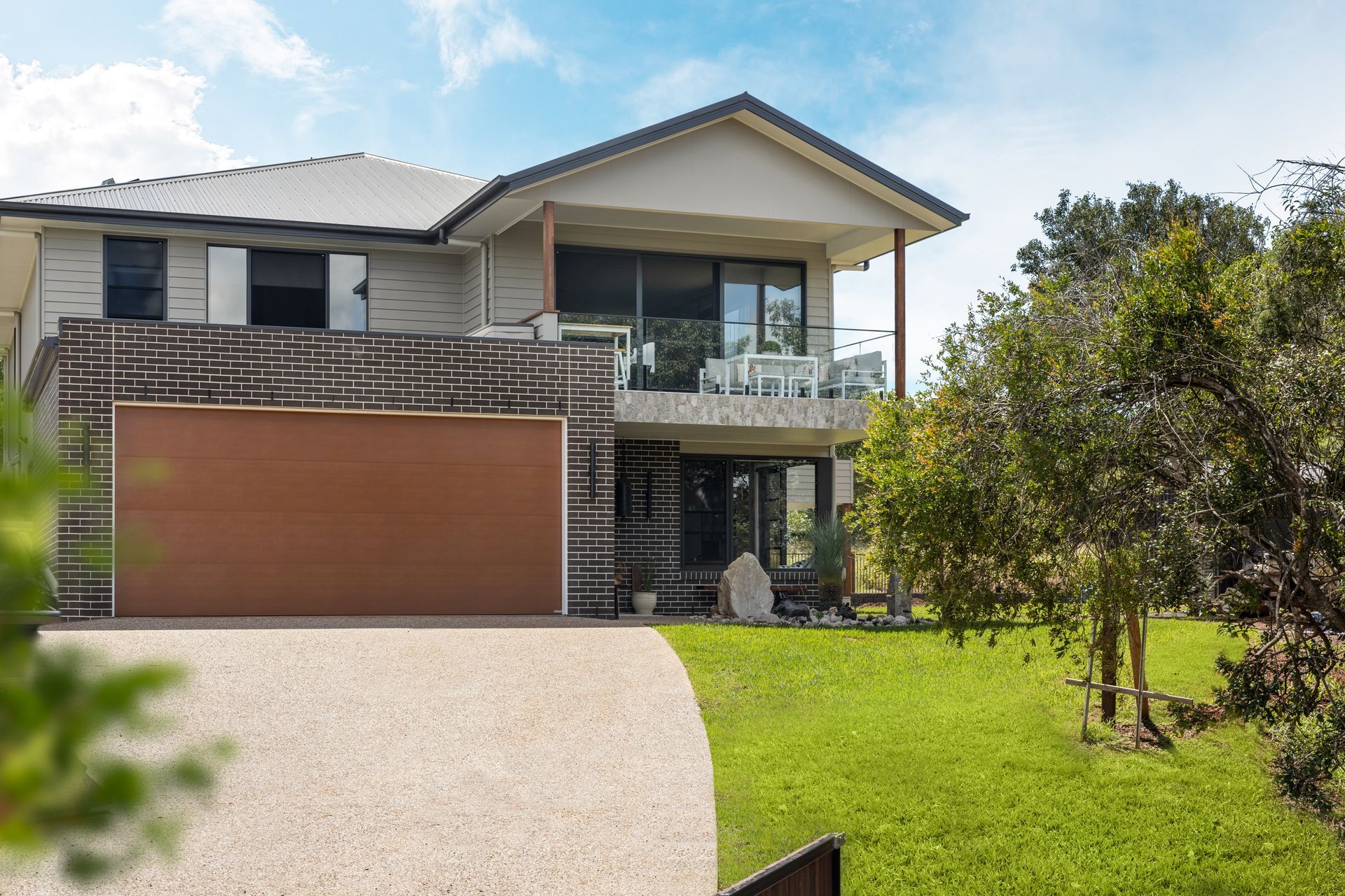 a large house with a brown garage door is sitting on top of a lush green hillside .