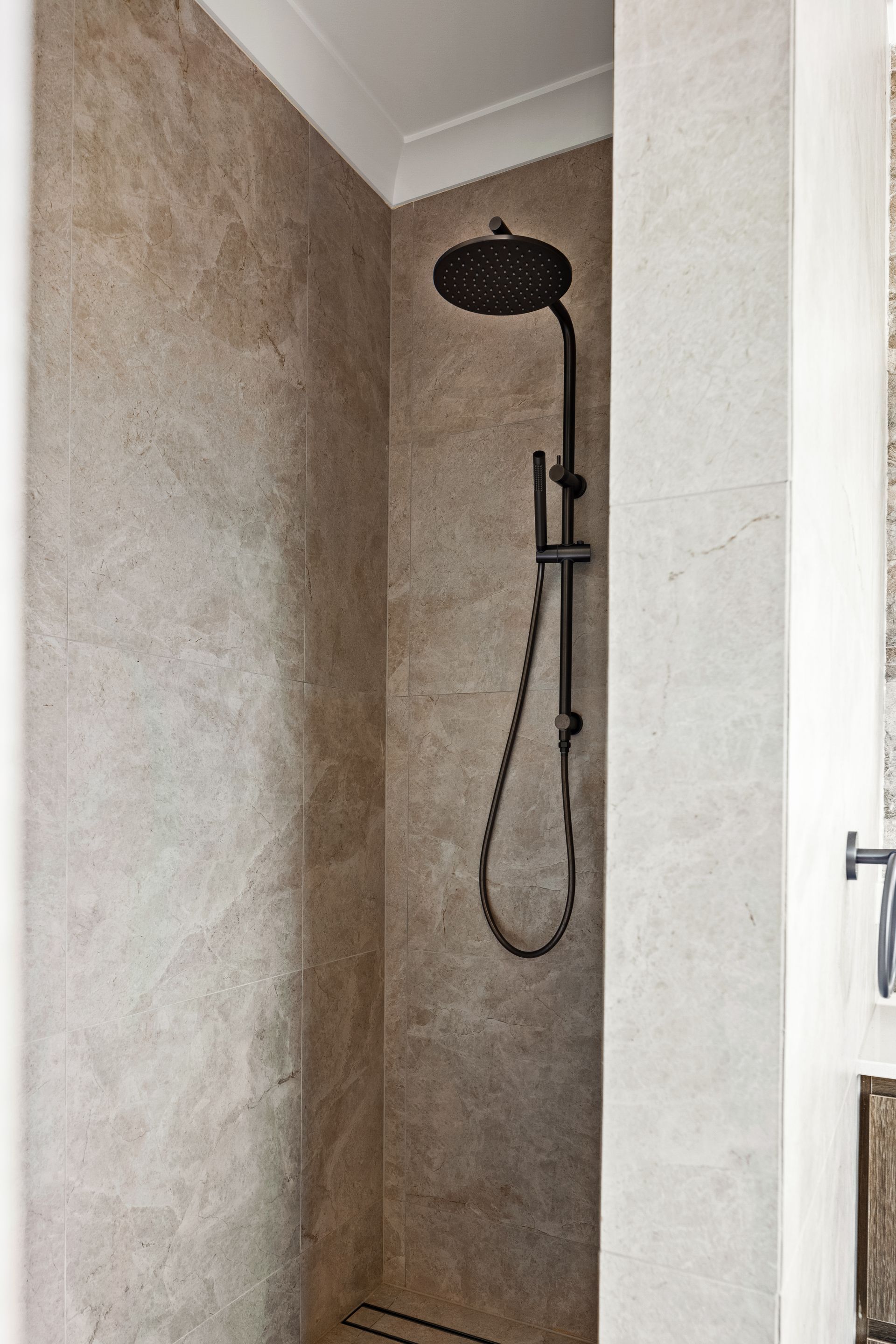 a shower with a black shower head and hose in a bathroom .