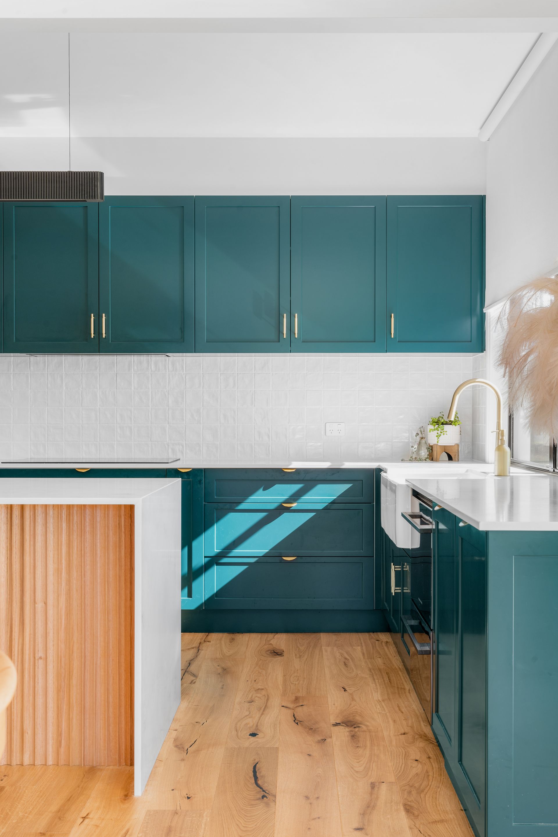 a kitchen with green cabinets , white counter tops , and wooden floors .