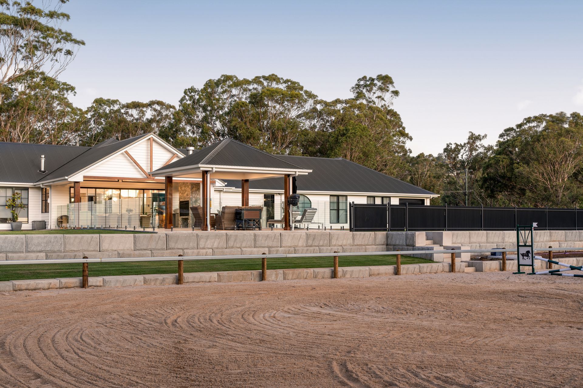 a large white house with a black roof is surrounded by trees and a dirt field .