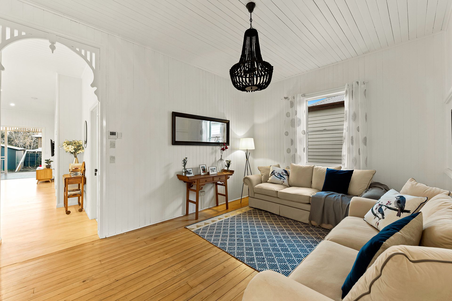 a living room with a couch , table , mirror and chandelier .