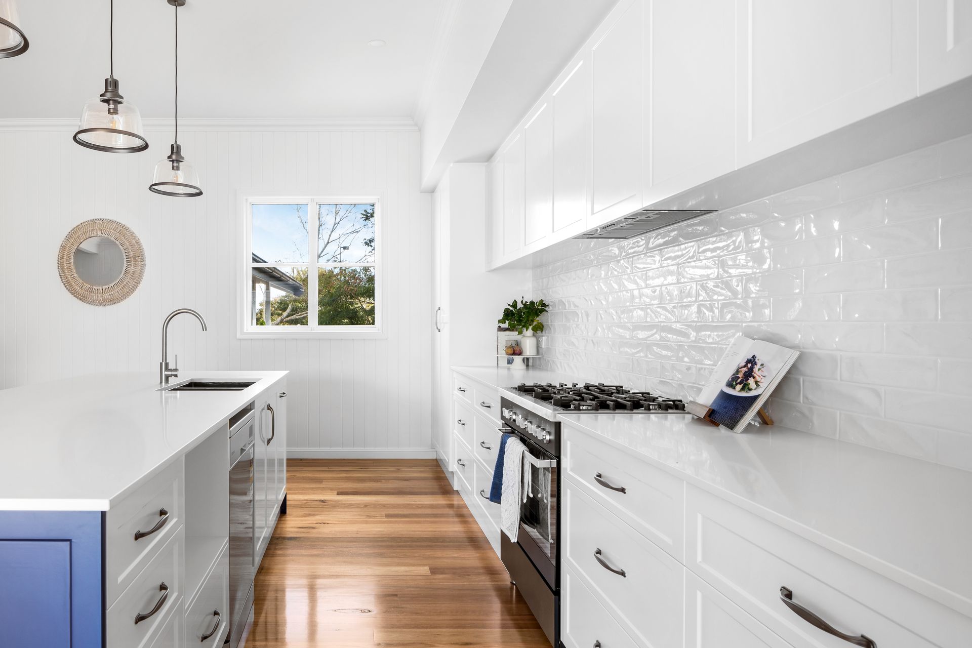 a kitchen with white cabinets , wooden floors , a stove and a sink .
