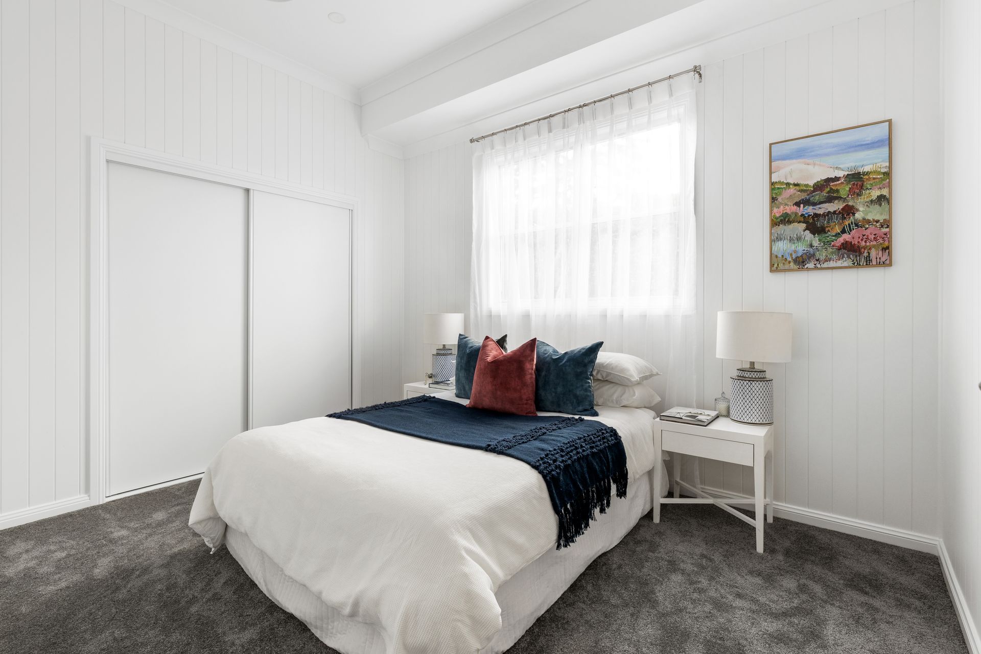 a bedroom with a bed , nightstand , lamps and a painting on the wall .