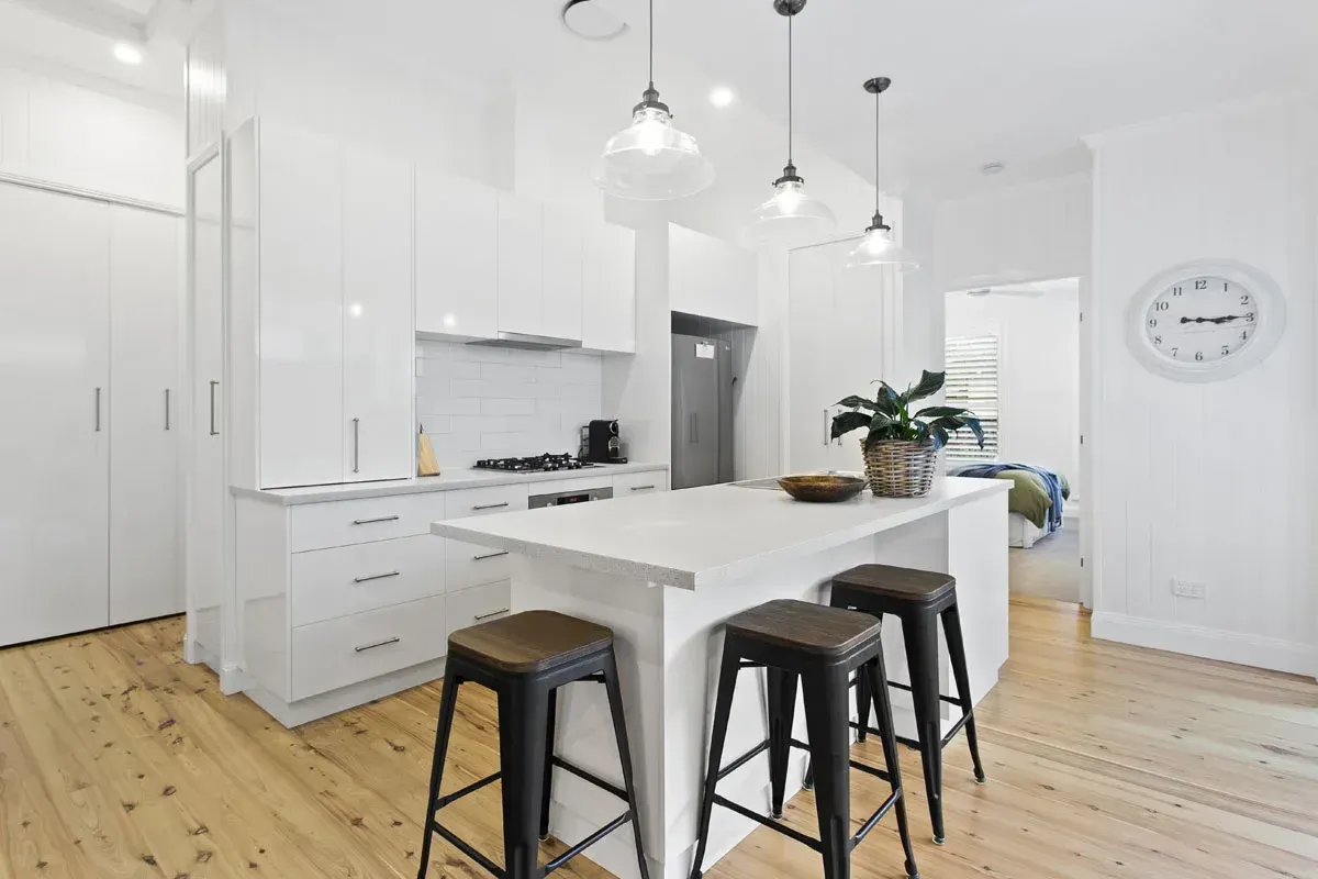 a kitchen with white cabinets , wooden floors , stools and a large island .