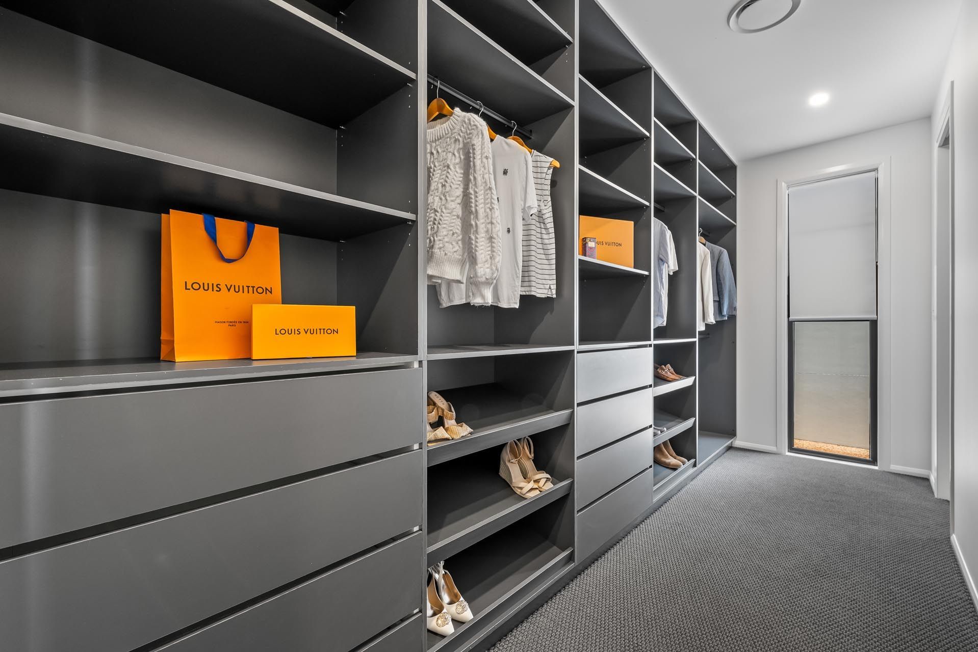 A walk in closet with lots of shelves and drawers filled with clothes and shoes.
